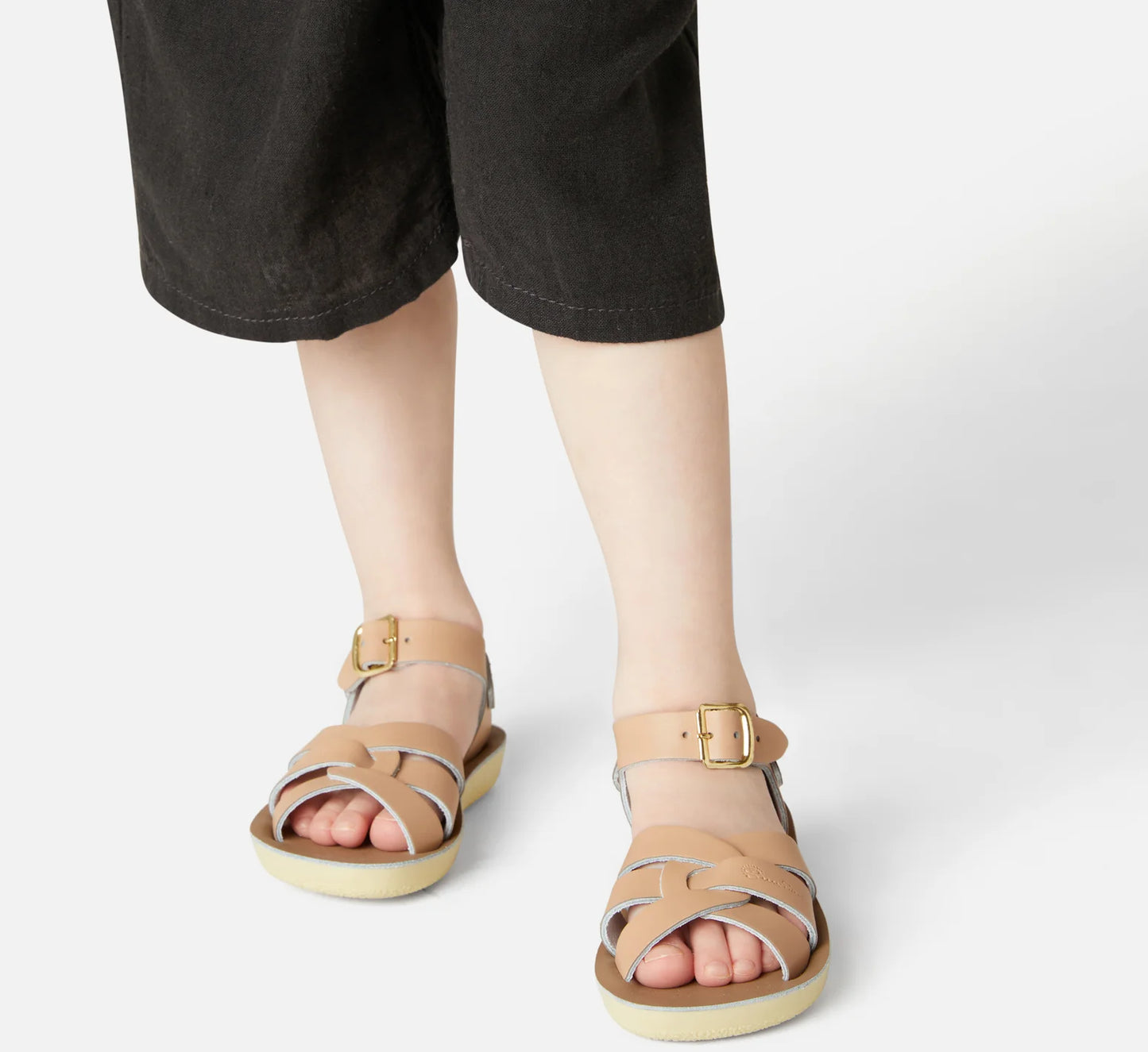 A unisex sandal by Saltwater, style swimmer in Latte with gold buckle strap. Image of child modelling the sandals