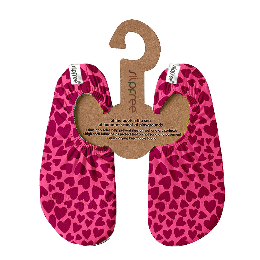 A pair of swim shoes by Slipfree, style Melissa in pink with dark pink love heart pattern, hanging on carboard hanger