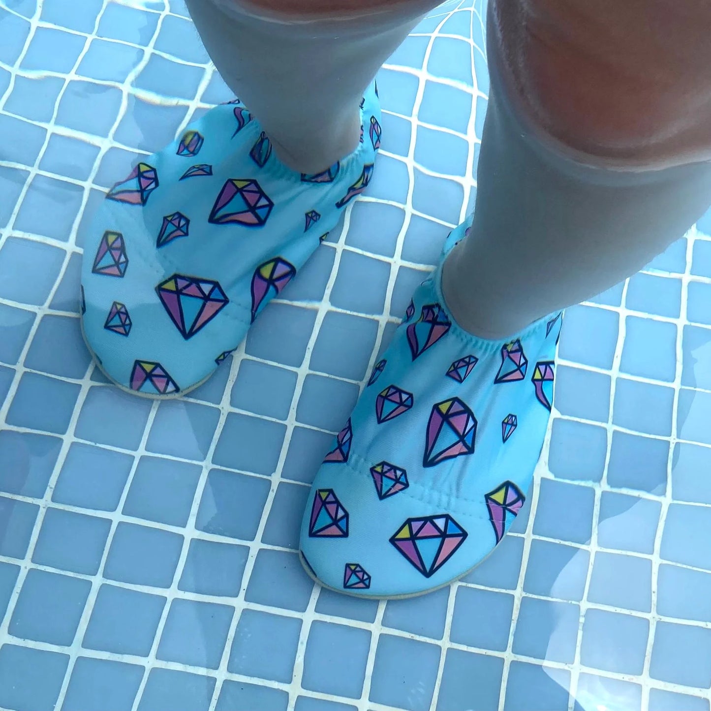 A pair of non-slip swim shoes by Slipfree, style Titan, in pale blue and multi gem stone print. Lifestyle image.
