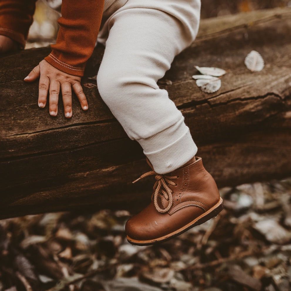 Tan leather shoe shown on child sat on a log.