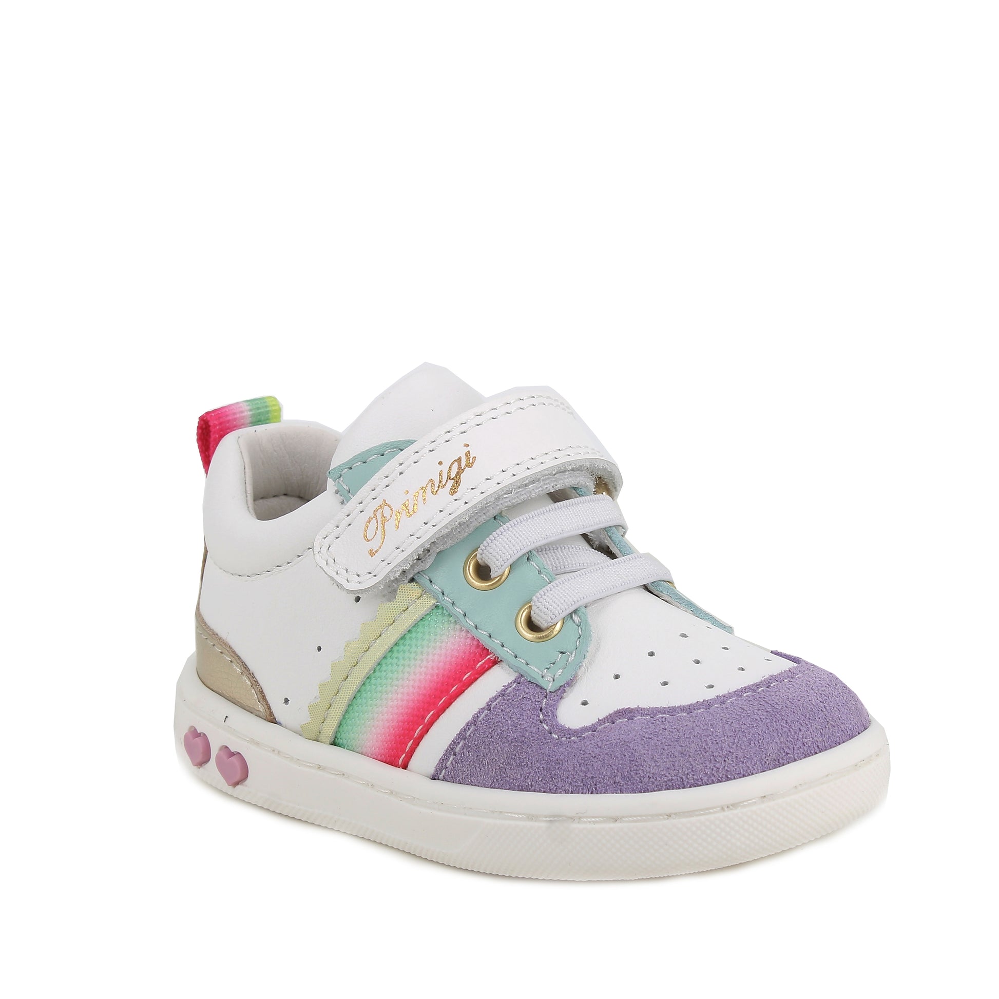 A girls casual trainer by Primigi, style Baby Like in white/iris with elastic laces and velcro strap. Rainbow stripe detail onside purple toe bumper pattern, and metallic design on heel. Two small pink love hearts on white sole. Angled front  view