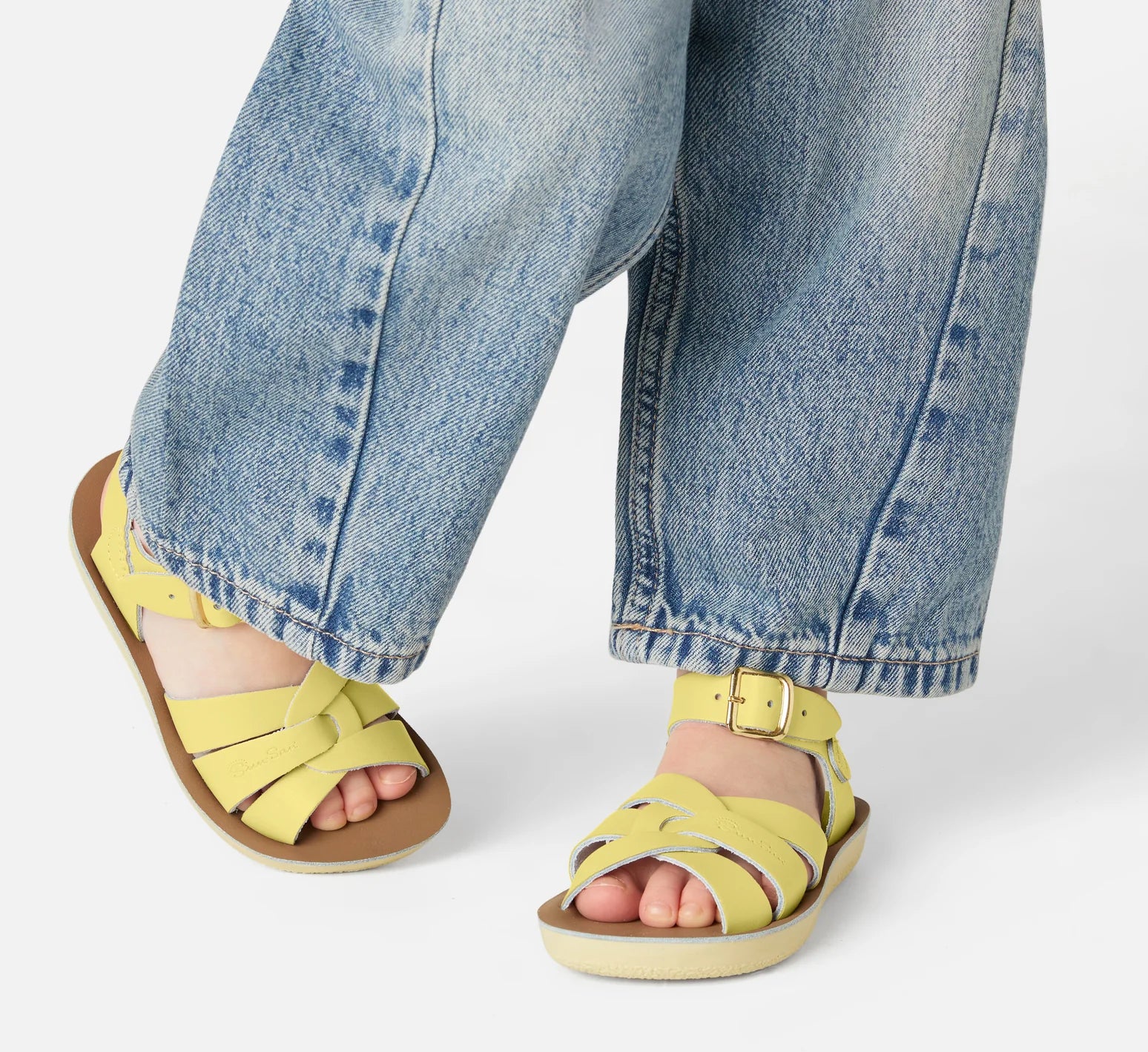 A girls sandal by Salt-Water, style Swimmer, in yellow with buckle fastening. Lifestyle image of girl wearing sandals with jeans. 