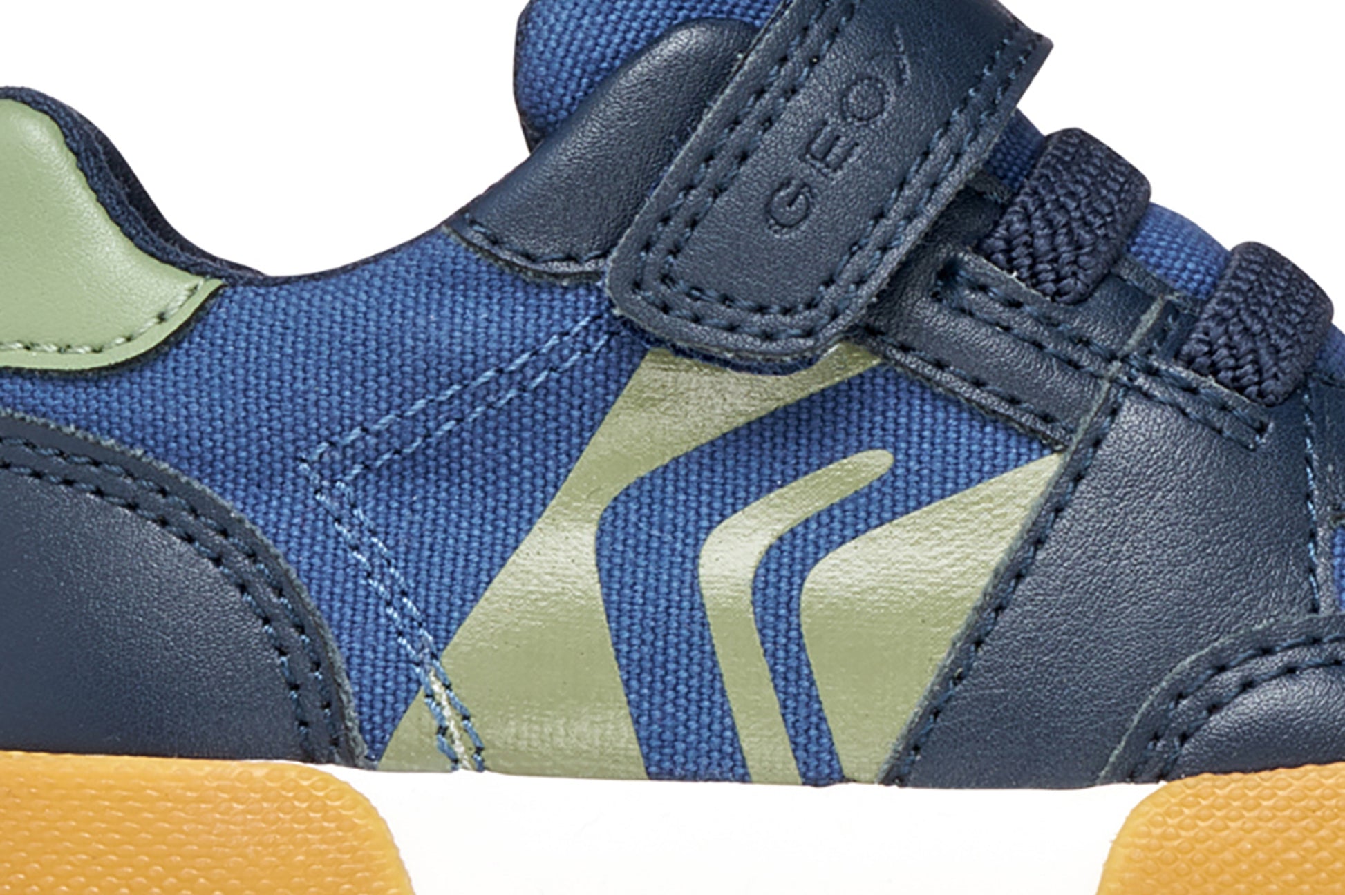 A boys casual shoe by Geox, style Gisli Boy in navy/olive with velcro strap and elastic laces with olive green pattern on side. Zoomed view of side pattern