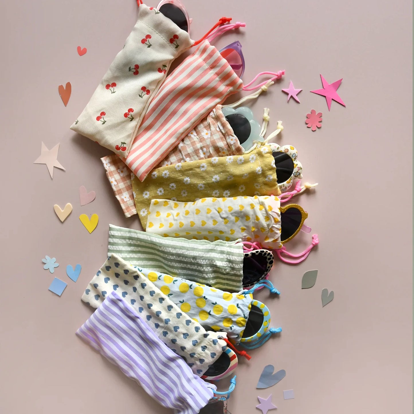 Colorful drawstring bags with sunglasses with various patterns by Rockahula on a light pink background with confetti