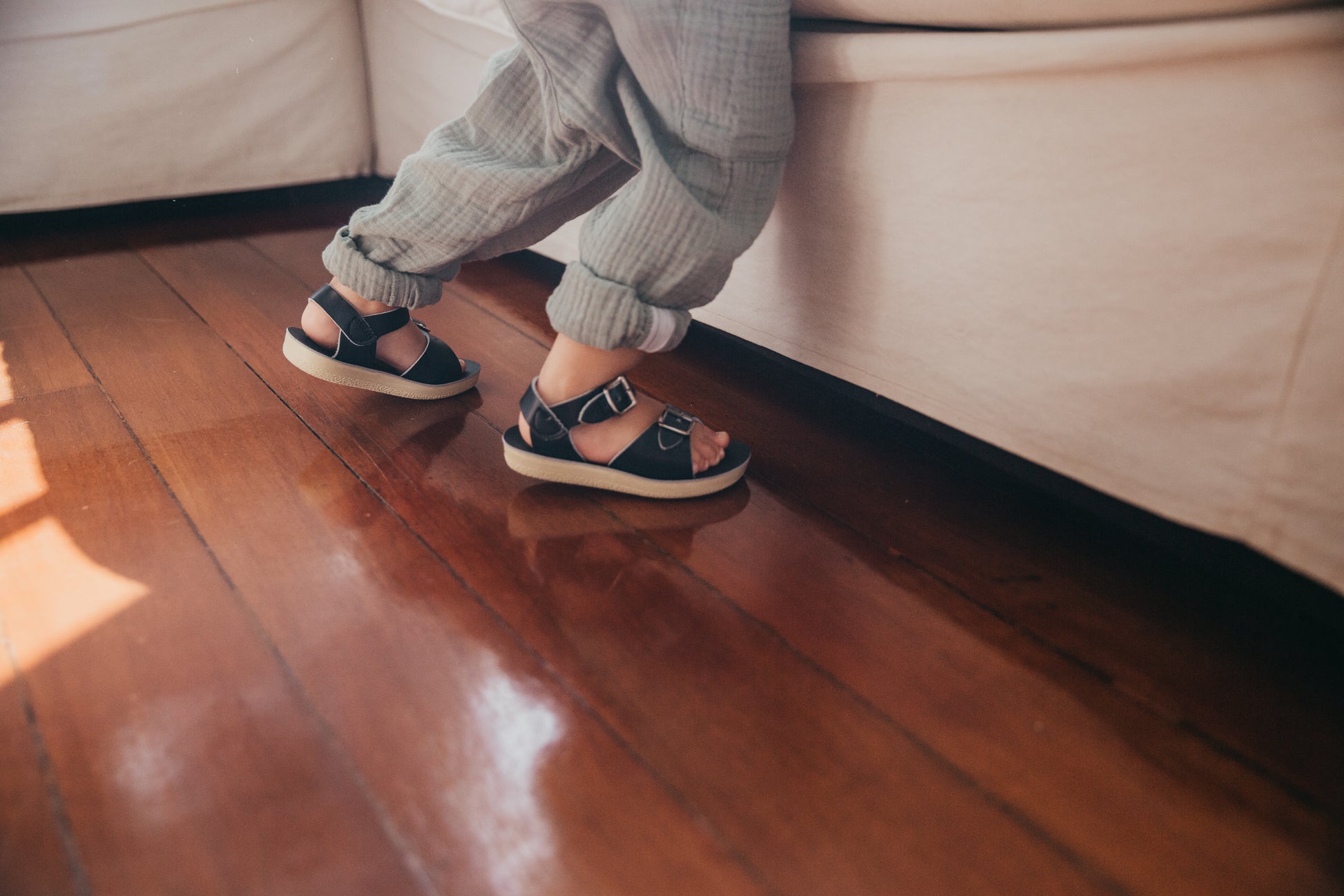 A unisex sandal by Salt Water Sandals in navy with double buckle fastening across the instep and around the ankle. Open Toe and Sling-back. Lifestyle of boys legs climbing onto couch..