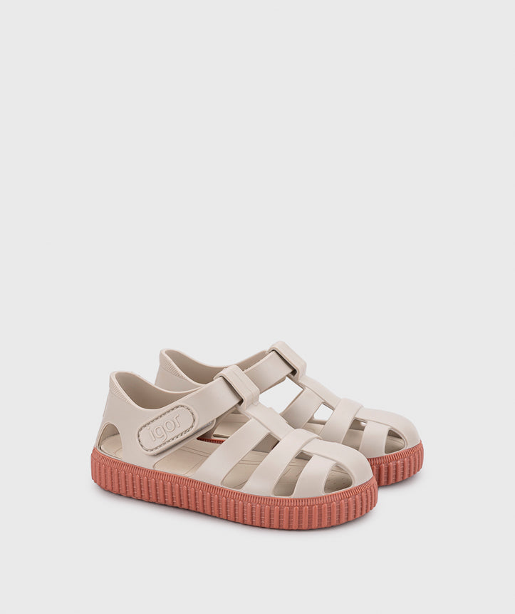 A girls sandal by Igor, style Nico in sand/terracota with velcro strap and pink sole. Angled side view of pair