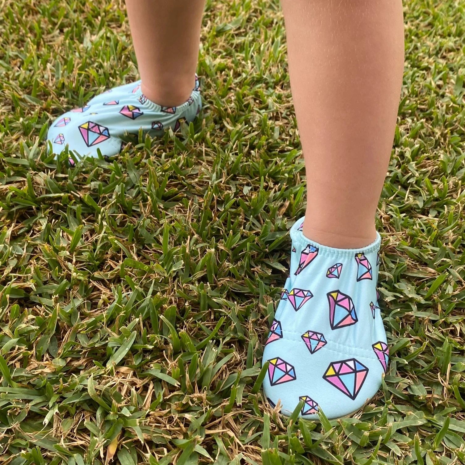A pair of non-slip swim shoes by Slipfree, style Titan, in pale blue and multi gem stone print.  Lifestyle image.