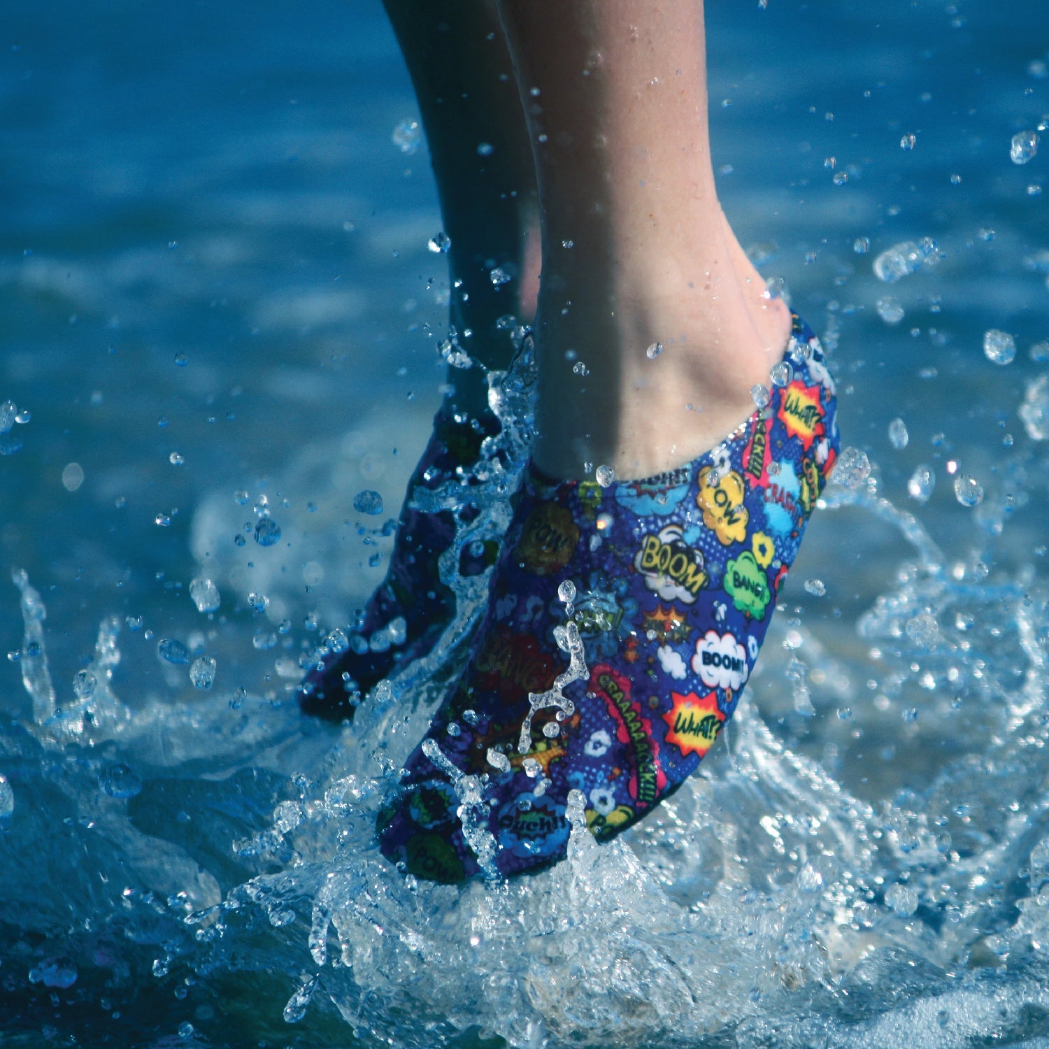 A boys non slip swim shoe by Slipfree, style Superhero, in Royal Blue with onomatopoeia print. Boy jumping in the pool view 