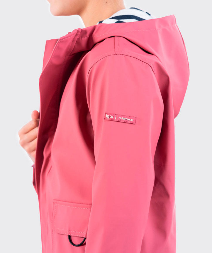 A girls hooded rain coat by Igor, style Euri, in pink with pockets and navy and white stripe lining. Lifestyle image.