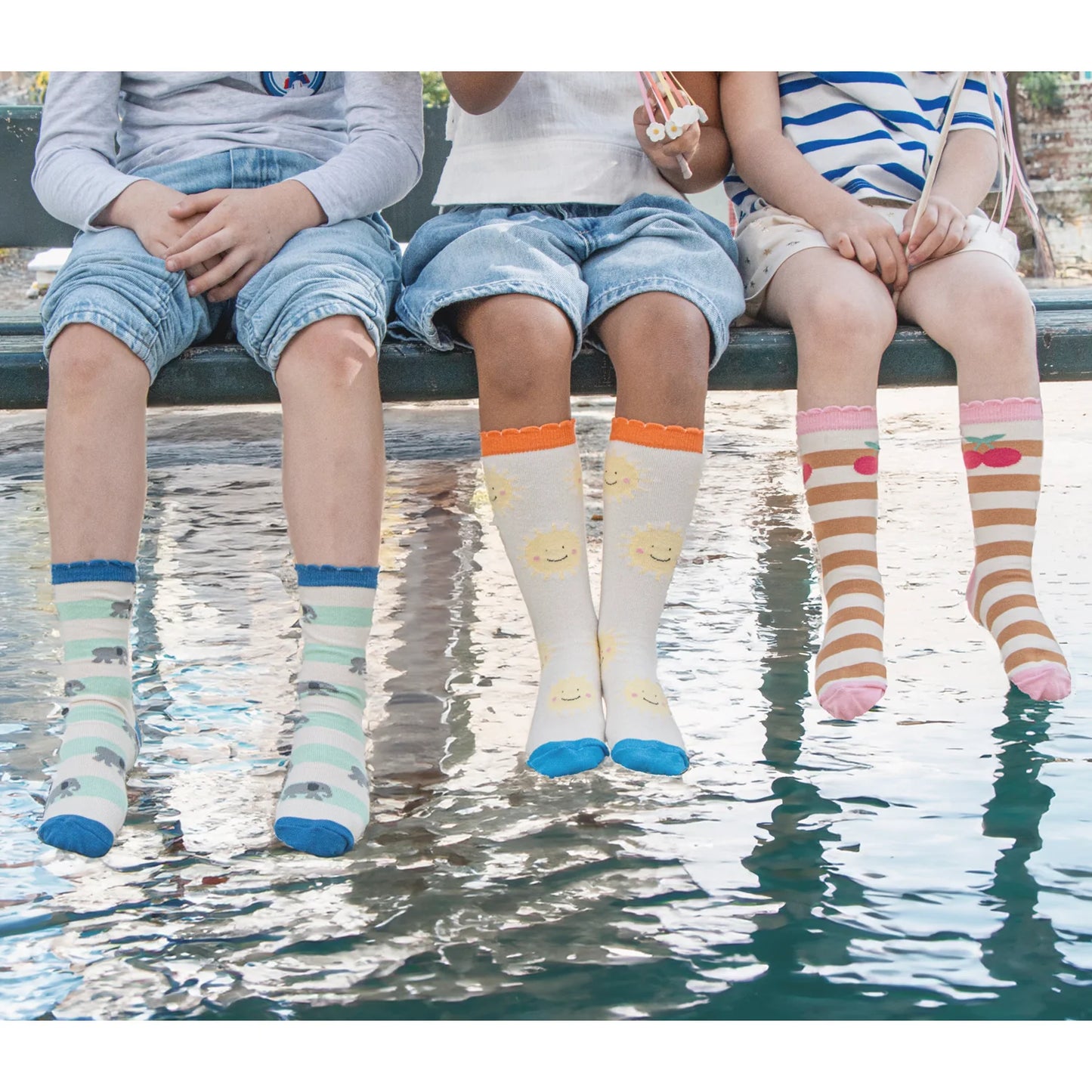 Three children sitting by a body of water wearing colorful socks by Rockahula