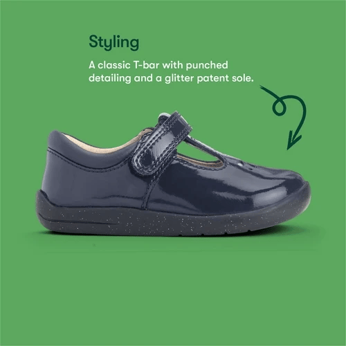 A girls t-bar shoe by StartRite, style Puzzle in patent navy, with flower design on the front and glitter in a black sole. Side view on green background with text describing style of shoe