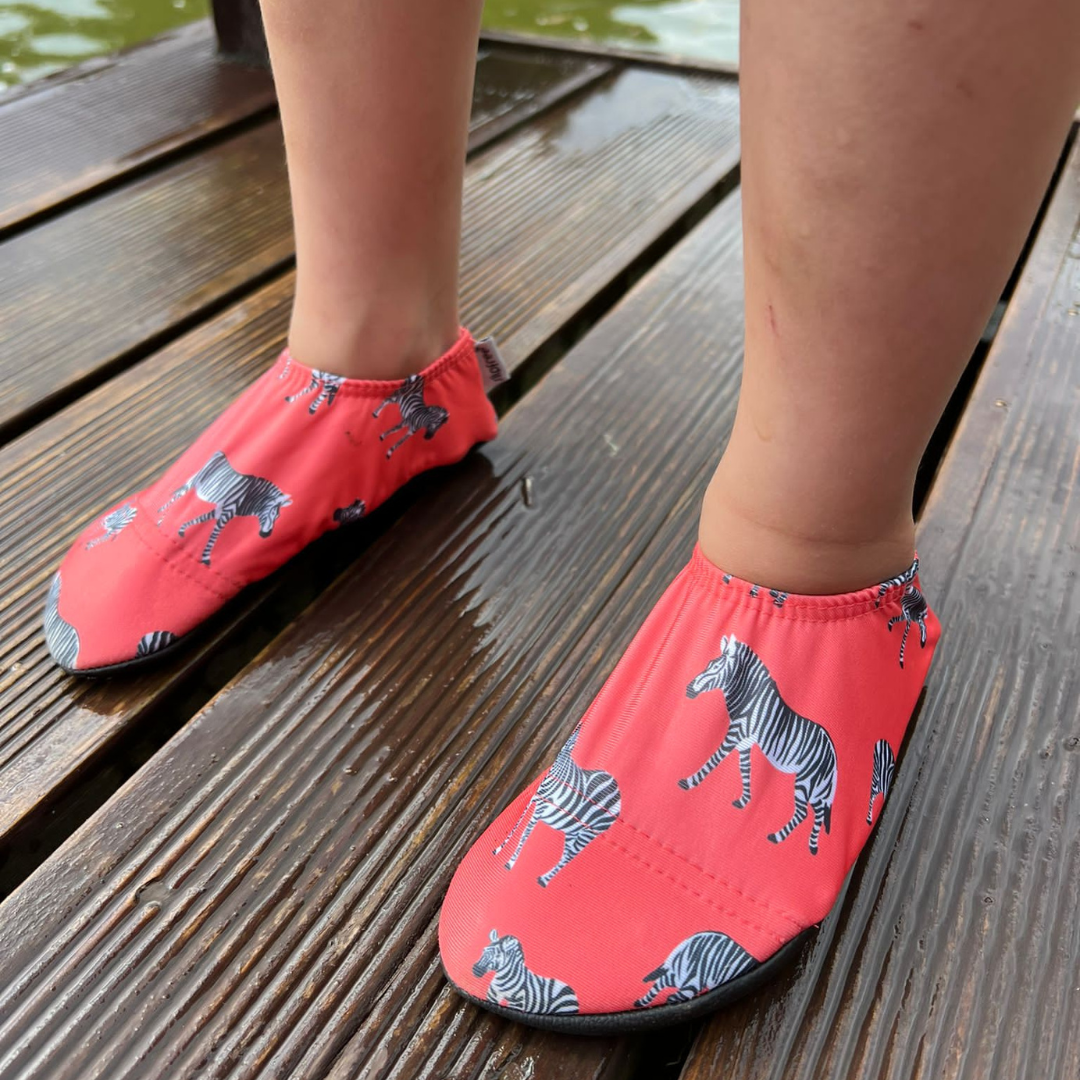 A girls non slip swim shoe by Slipfree, style Grevy, in coral with Zebra print. Lifestyle image.